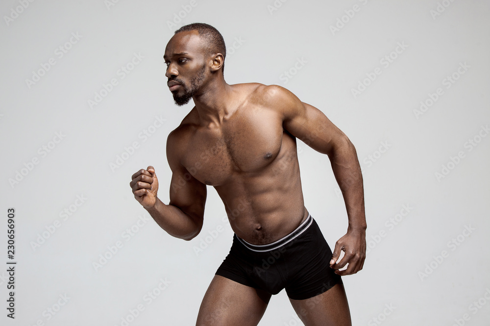 Fit young man with beautiful torso, isolated on gray background. The naked torso of African American man posing at studio. The muscular body, fitness, sports, healthy lifestyle and bodybuilder concept Fit young man with beautiful torso, isolated on gray background. The naked torso of African American man posing at studio. The muscular body, fitness, sports, healthy lifestyle and bodybuilder concept