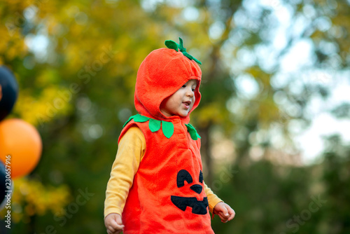 The boy dressed in an orange pumpkin costume at the Halloween party outside with black and orange balloons close up portrait 