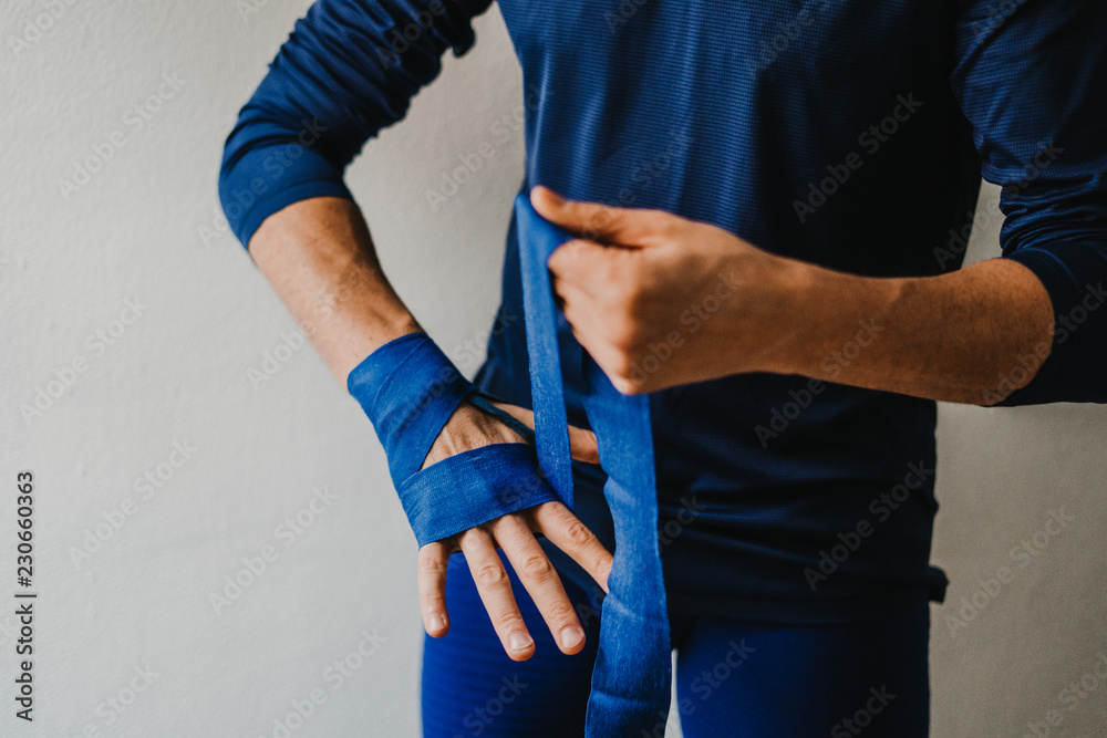 .Young sportsman man preparing bandages for his hands to start boxing. Sportwear in colour blue. Lifestyle..