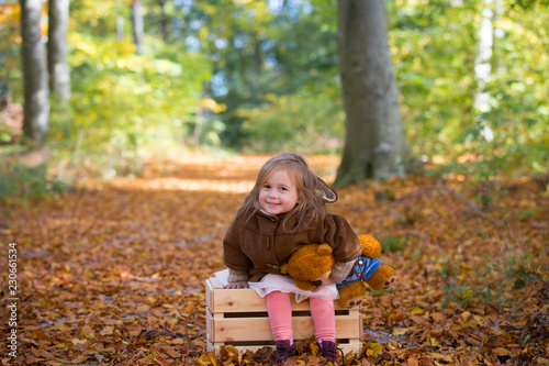 Adorable little girl in the forest with her teddy bear sitting on a wooden chest © 221anika