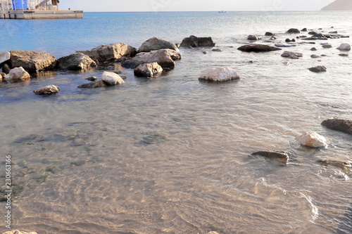 Sea shore with stones and rocks in reflected water at sunset on the horizon and harbor