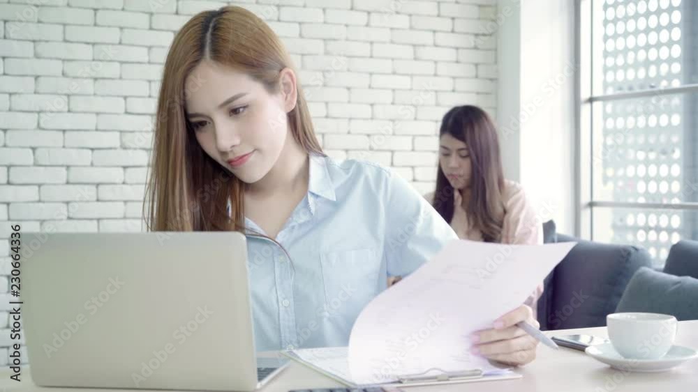 Attractive smart creative Asian business women in smart casual wear working on laptop while sitting on desk on office desk. Women work at office concept. Attractive smart creative Asian business women in smart casual wear working on laptop while sitting on desk on office desk. Women work at office concept.