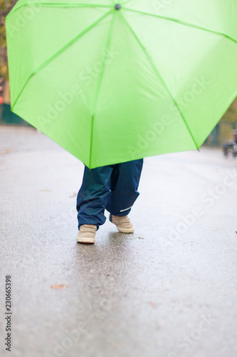 Little kid with green umbrella on wet road. Kleines Kind spielt mit grünem Regenschirm auf nasser Straße.