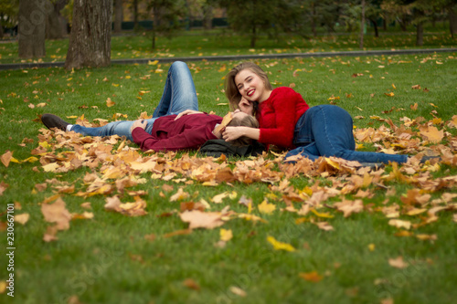 the girl and the guy in red sweaters and jeans sit in the park on the green grass in the yellow maple leaves, the girl smiles. a date in the fall.