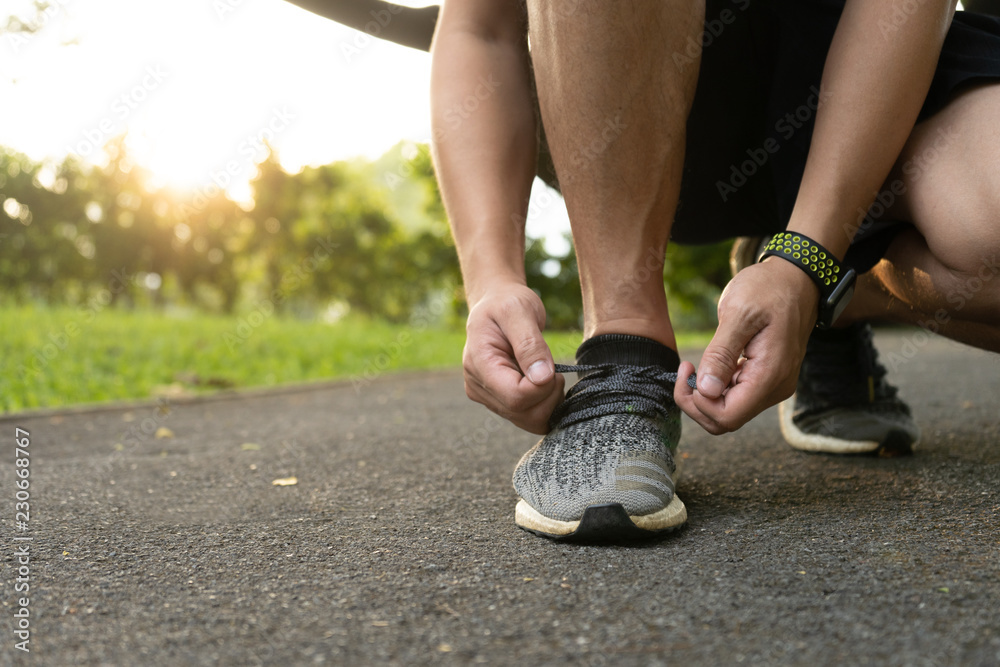 Closeup of feet of man runner getting ready tying running shoes before running in park exercising outdoors Closeup of feet of man runner getting ready tying running shoes before running in park exercising outdoors