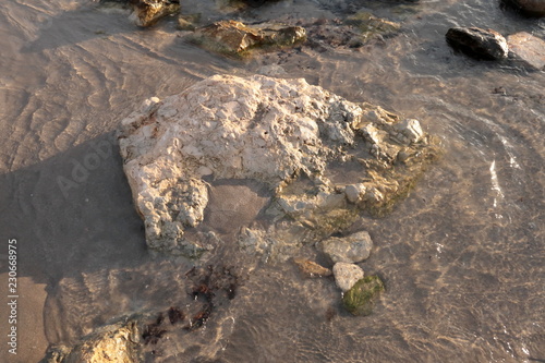 Sea shore with sand and stones and rocks in the water at sunset, close-up