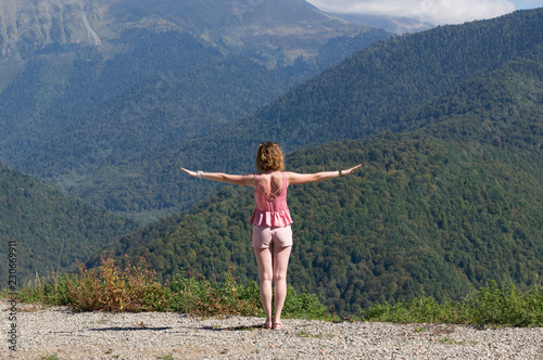 The girl traveler stands arms outstretched in the mountains