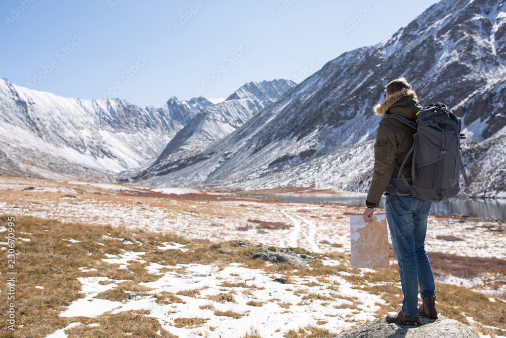 man stands on a background of mountains and holds a map in his hand