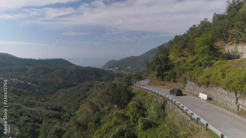 Aerial: Winding and curvy mountain road going through forests Small Town in the background Italy Aerial: Winding and curvy mountain road going through forests Small Town in the background Italy