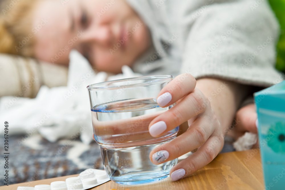 Young woman suffering from headache, cold and flu is holding a glass of water