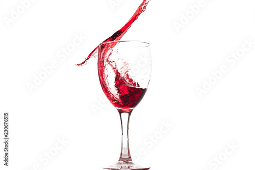 Red wine falls into a glass and creates splash and splashes on a white background.