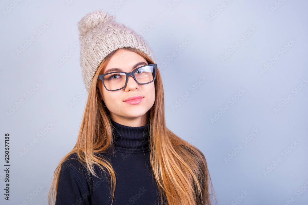 Young beautiful girl with glasses and winter hat standing in front of grey background, a lot of clean space Young beautiful girl with glasses and winter hat standing in front of grey background, a lot of clean space