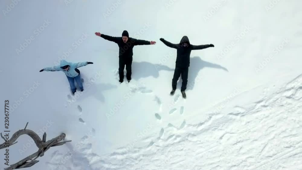 Three people throws themselves into the snow and make snow angels. Aerial shot. Three people throws themselves into the snow and make snow angels. Aerial shot.