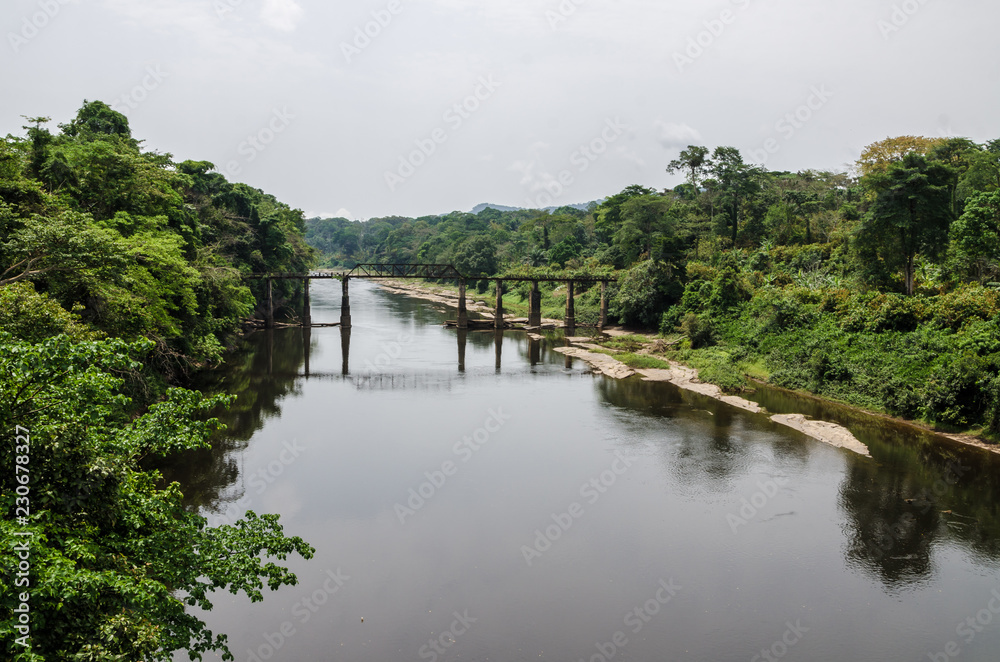 Crumbling iron and concrete bridge crossing Munaya river in rain forest of Cameroon, Africa.