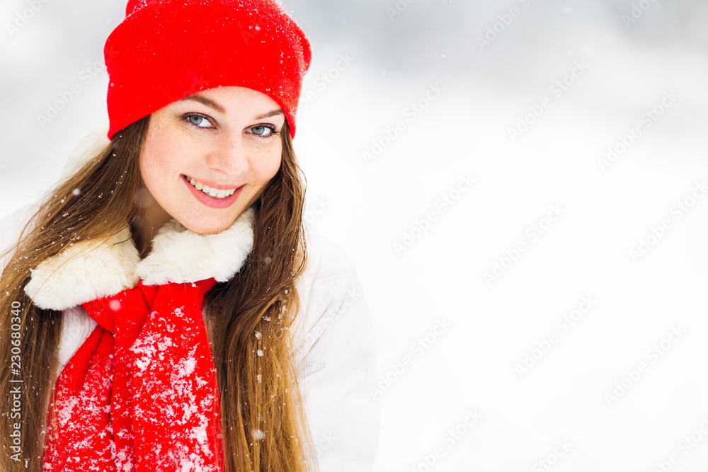 close-up of girl in winter jacket and red hat with scarf on which there is snow. she cute smiles and looks at the camera lens close-up of girl in winter jacket and red hat with scarf on which there is snow. she cute smiles and looks at the camera lens