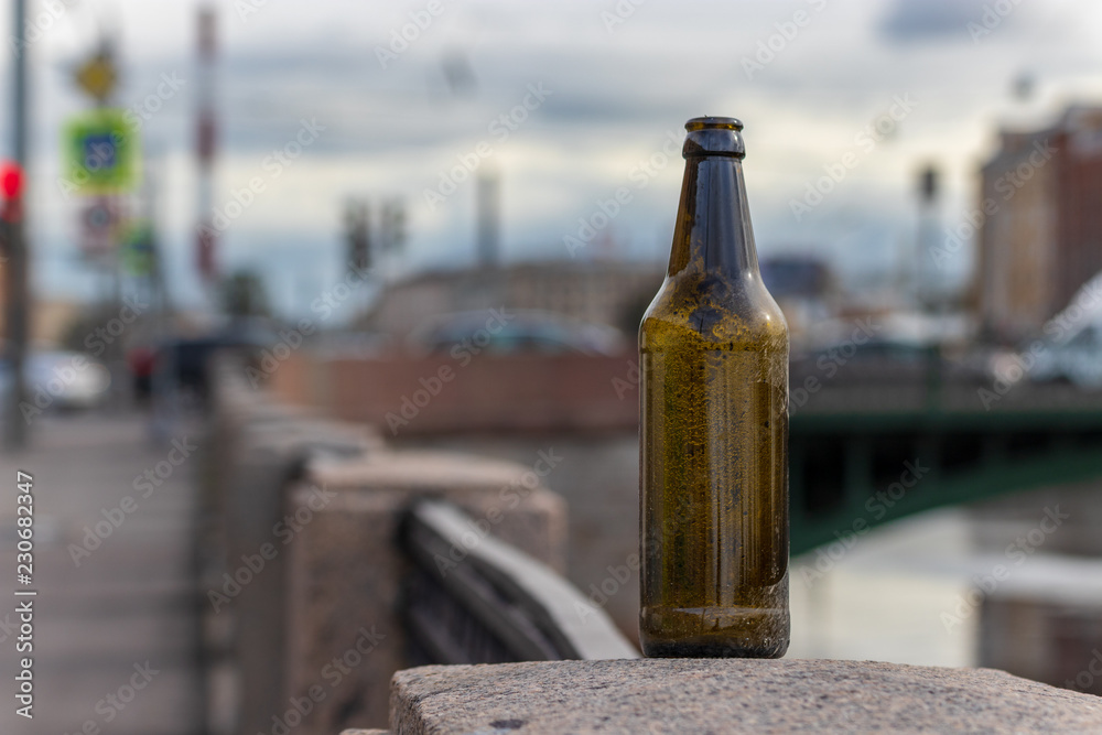 Drinking alcohol in the city. Problems thrown in the wrong place garbage. A bottle of beer stands on the parapet of the embankment