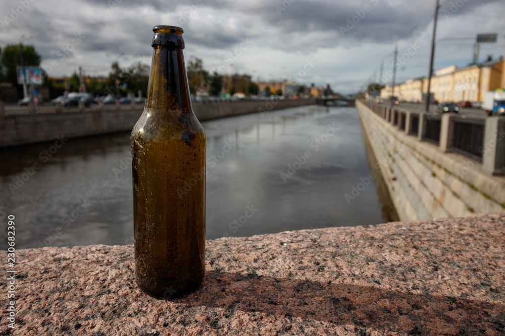 People leave trash in the wrong place. A beer bottle on the granite parapet of the embankment of a city canal or river. People leave trash in the wrong place. A beer bottle on the granite parapet of the embankment of a city canal or river.