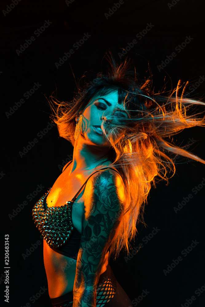 Alternative model with bangs and colored hair poses under teal and orange light wearing a fishnet top