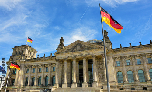 German flags waving in the wind at famous Reichstag building  seat of the German Parliament  Deutscher Bundestag   on a sunny day with blue sky and clouds  central Berlin Mitte district  Germany.