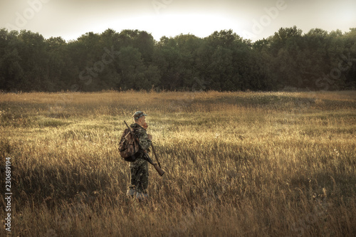 hunter hunting in  rural field nearby woodland at sunset during hunting season