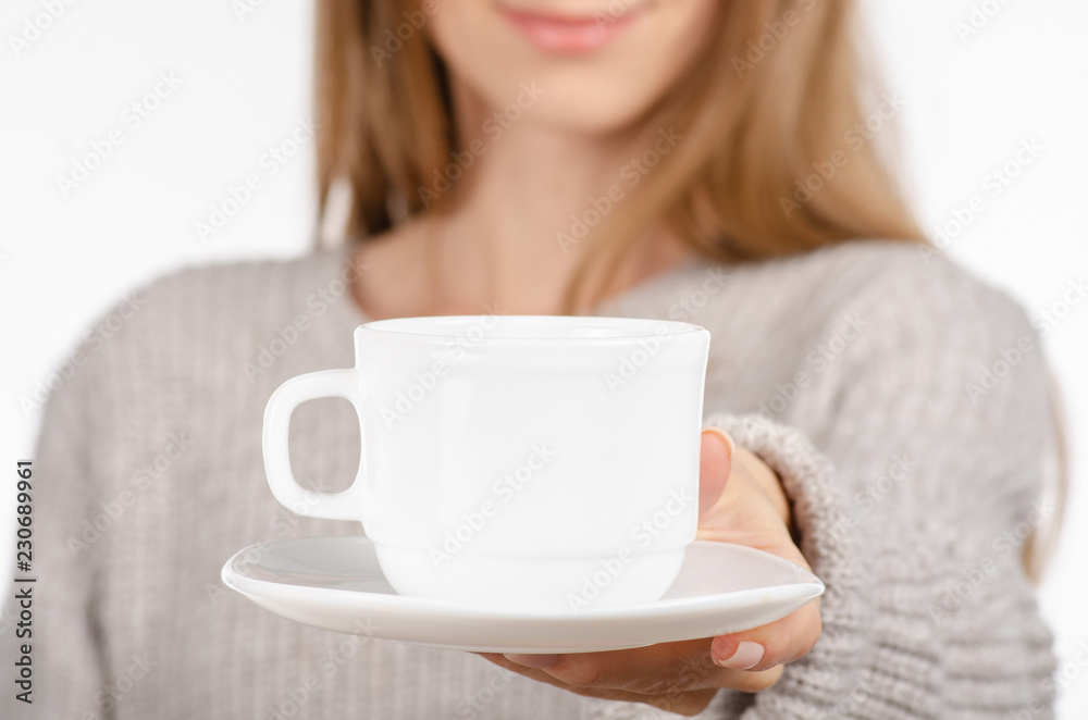 Young woman in sweater holding a white cup and saucer in hands, drinking hot coffee on white background. Space for your logo or text. Young woman in sweater holding a white cup and saucer in hands, drinking hot coffee on white background. Space for your logo or text.