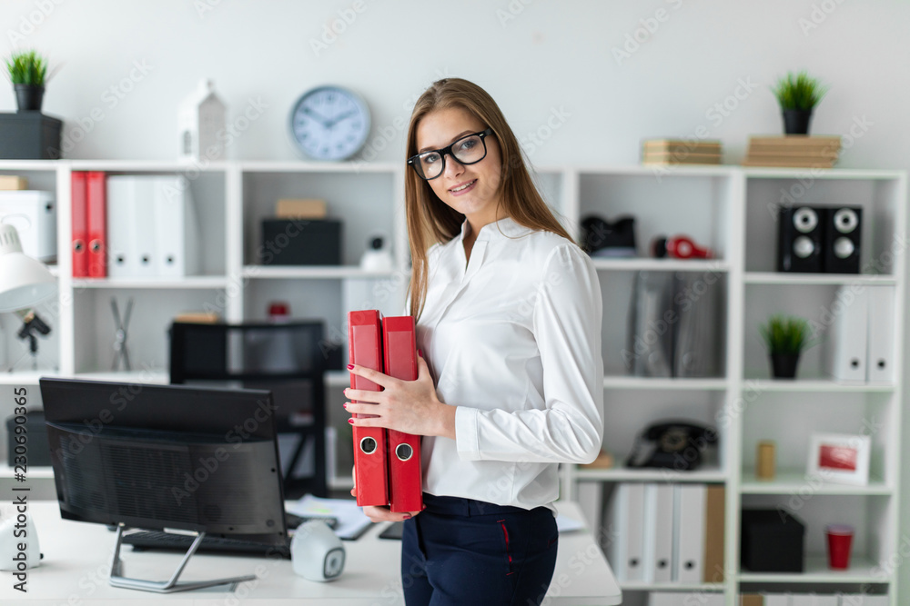 A young girl stands near a computer Desk and holds a folder with documents A young girl stands near a computer Desk and holds a folder with documents