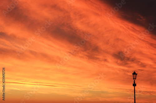 Sunset Sky Background with Orange and Yellow Sky Colors and Street Lantern Silhouette. Scenic Sky Cloudscape at Sunset or Sunrise, Dusk and Dawn Nature Wallpaper, Beautiful Evening Sunset Scene © onajourney