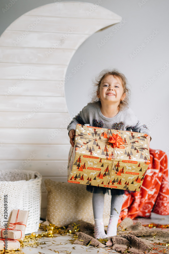Petite beautiful girl with modern clothes stands with a gift on the background of moon and a basket adorned under the new Year Petite beautiful girl with modern clothes stands with a gift on the background of moon and a basket adorned under the new Year