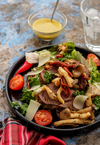 Salad with warm beef with oyster mushrooms, tomatoes and greens.