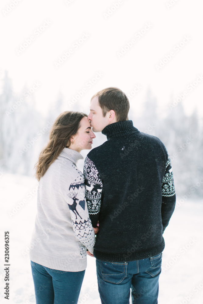 Fototapeta premium happy loving couple walking in snowy winter forest, spending christmas vacation together. Outdoor seasonal activities. Lifestyle capture.