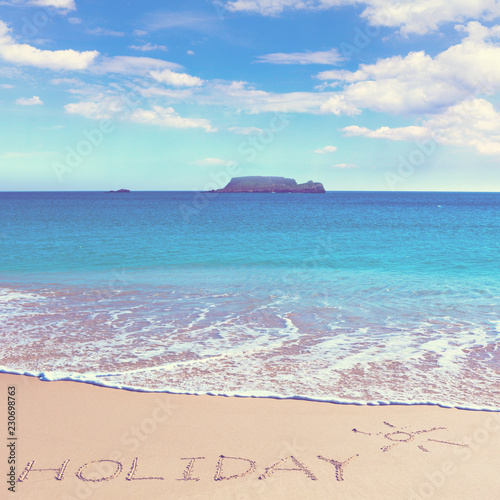 HOLIDAY insctiption under the sun drawing on wet beach sand with the turquoisesea and the island on background photo