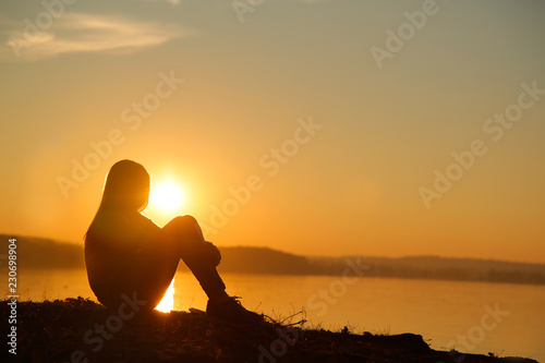 Teen sitting on the beach and watching the sunset