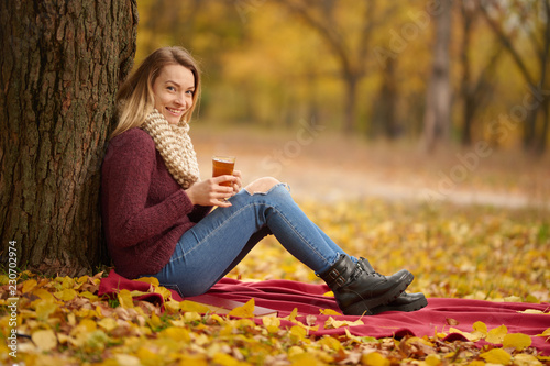 Girl in the autumn park on a warm blanket and with hot tea. Concept of autumn warmth, atmosphere and comfort. With space for an inscription