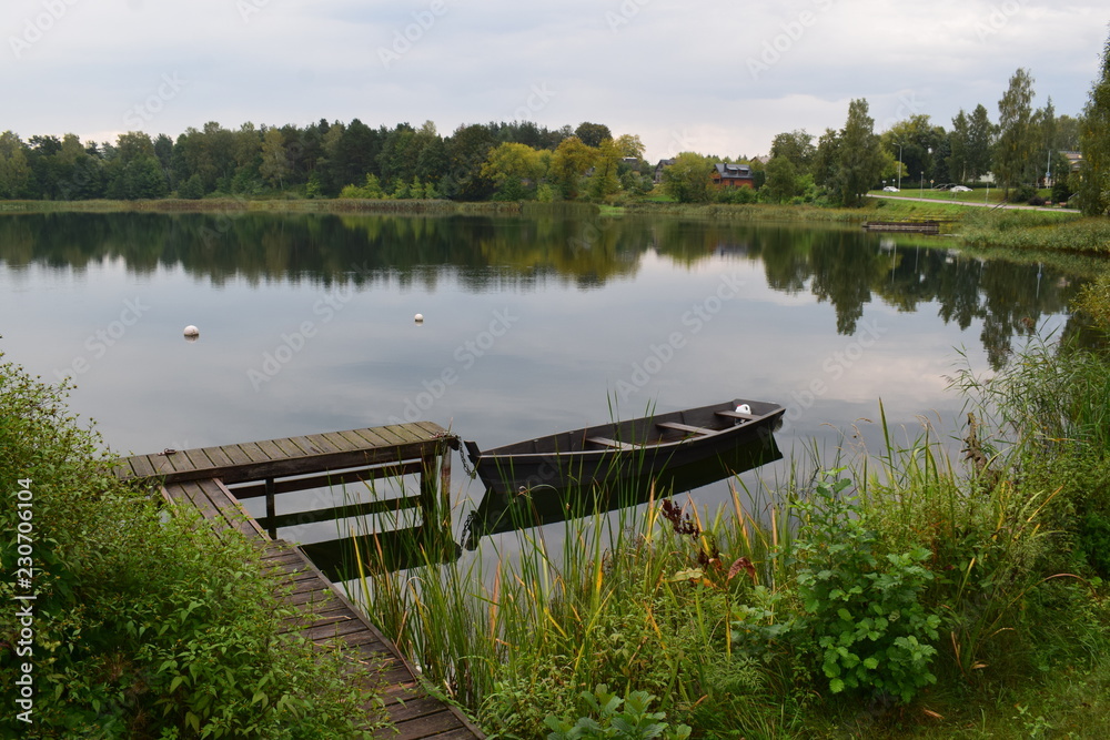 Beautiful landscape. Wooden bridge with boat. Lake, forest, shore, sky. Reflection in water.