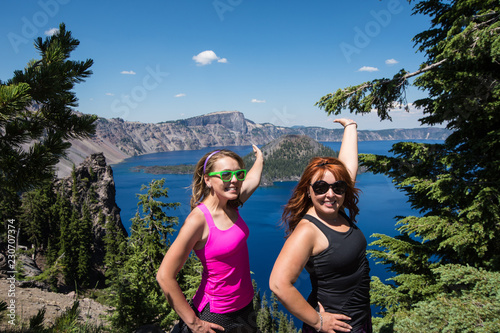 Two women friends (20s) smile and pose, holding arms out at Crater Lake National Park in Oregon