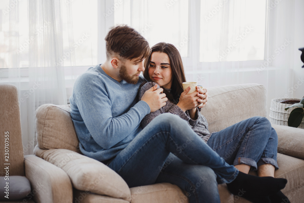 Young couple sitting at sofa with hot drinks. Love, relationships, conversation, winter weekend concept Young couple sitting at sofa with hot drinks. Love, relationships, conversation, winter weekend concept