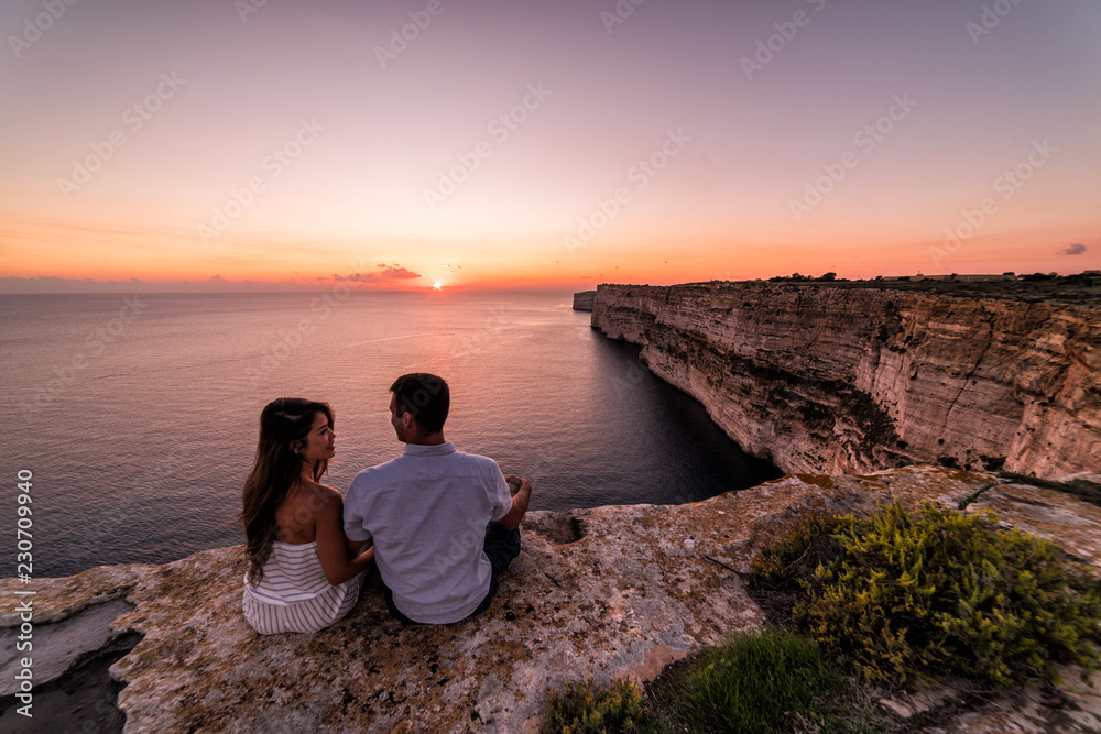 Couple overlooks the famous Ta Cenc Cliffs at sunset. These cliffs on the island of Gozo overlook the Mediterranean Sea. Country of Malta.