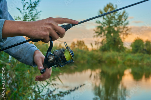 Lake at sunset. A fisherman on the bank. Fishing rod wheel closeup. Spinning reel. The concept of outdoor activities. Tackles for pike, perch, zander.