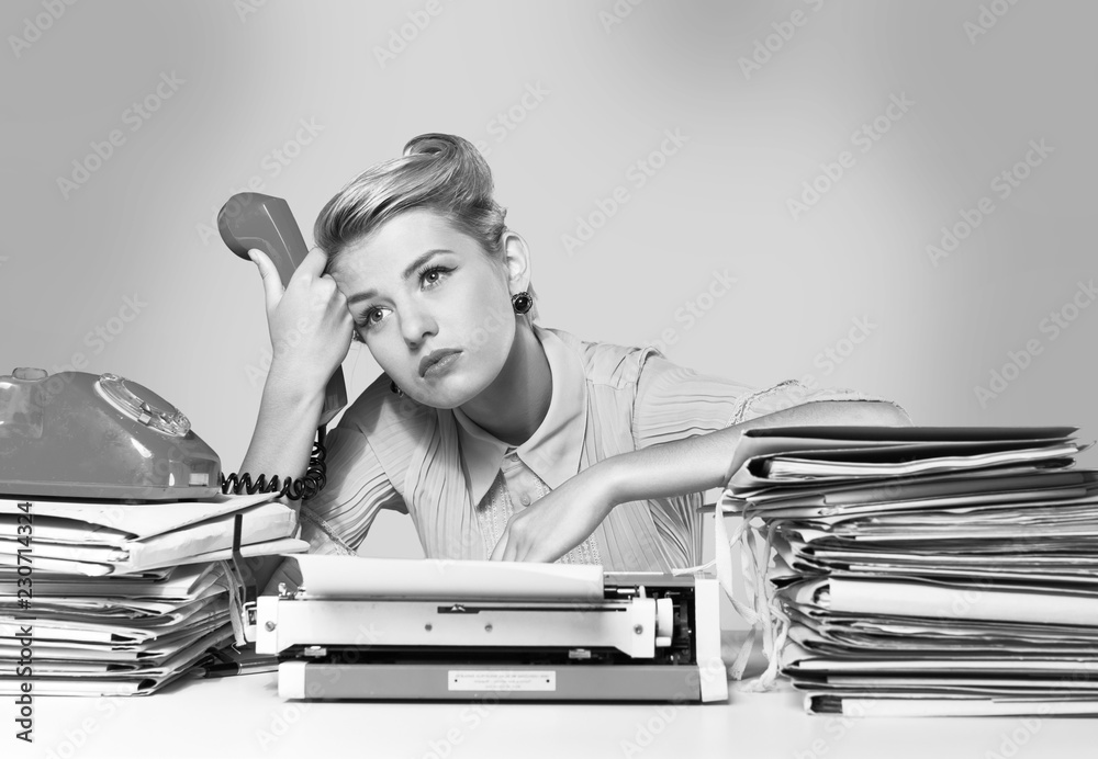 Fototapeta premium Young blonde female writer using typing machine, black and white