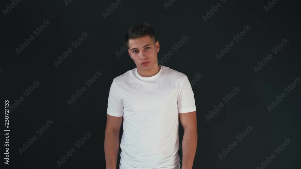 Portrait of attractive and handsome young man stands in white shirt and looks on camera. Isolated on black background Portrait of attractive and handsome young man stands in white shirt and looks on camera. Isolated on black background