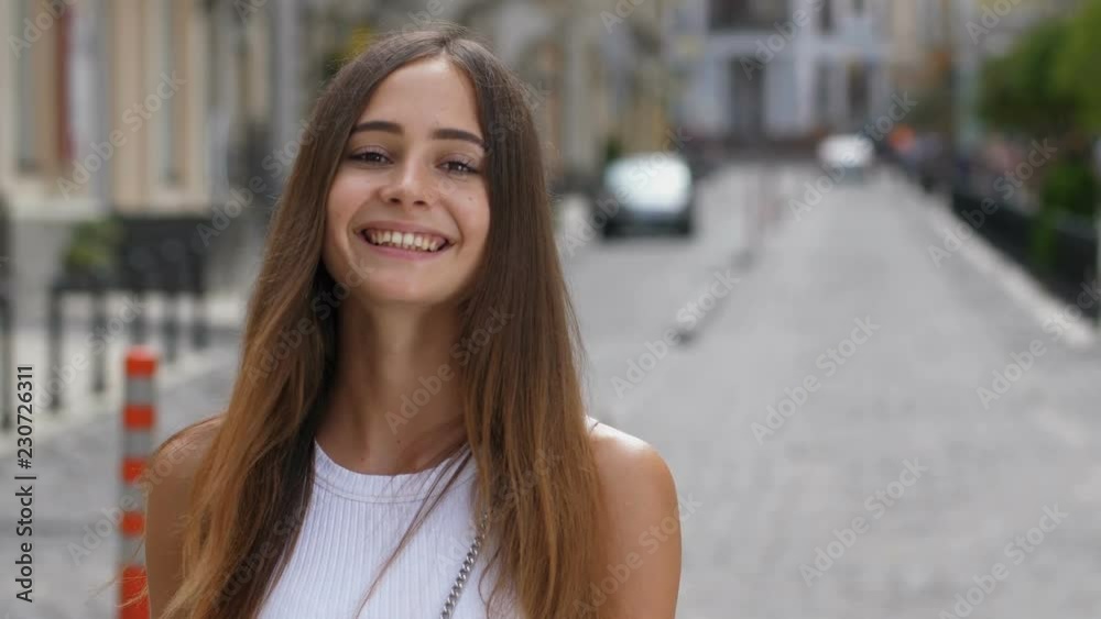 Portrait of gorgeous caucasian girl with long brown straight hair and deep brown eyes smiling at camera outdoors. Joyful young woman with clean tanned skin looking at you with innocent enigmatic smile Portrait of gorgeous caucasian girl with long brown straight hair and deep brown eyes smiling at camera outdoors. Joyful young woman with clean tanned skin looking at you with innocent enigmatic smile
