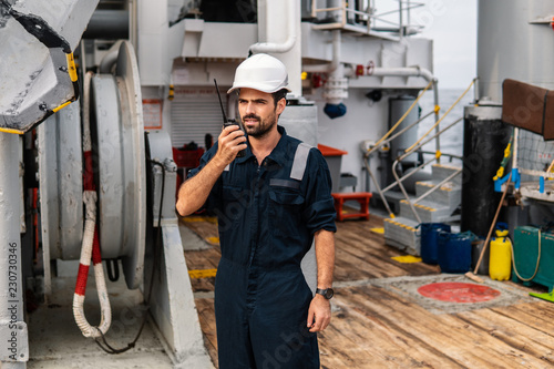 Marine Deck Officer or Chief mate on deck of vessel or ship . He holds VHF walkie-talkie radio in hands. Ship communication photo