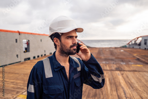 Marine Deck Officer or seaman on deck of vessel or ship . He is speaking on the mobile cell phone photo