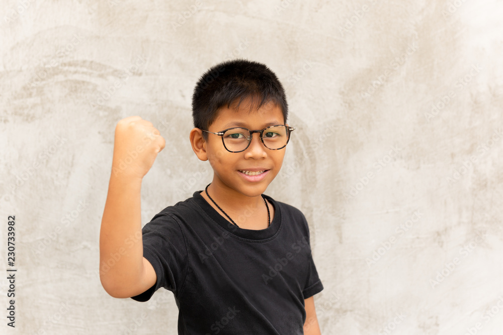 Asian boy with glasses hands up and smiling over grey background.