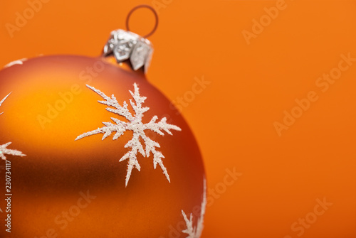 An orange Christmas bauble decoration close up adorned with a silver white snow flake on an orange background with room for custom text.
