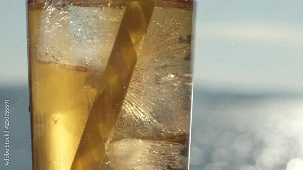 Close up Tilt down shot of a glass filled with ice and orange transparent liquid with yellow straw, Slowmo