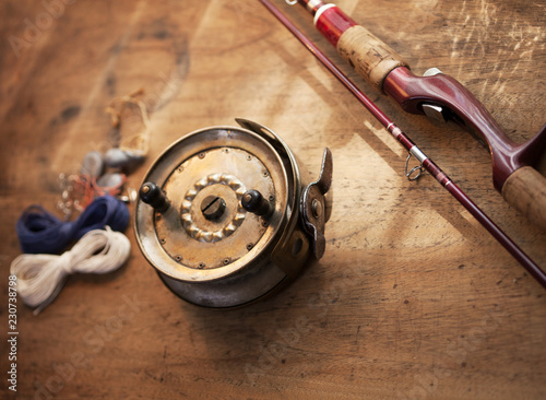 Vintage fishing reel, and rod on old wooden surface. Warm lighting.