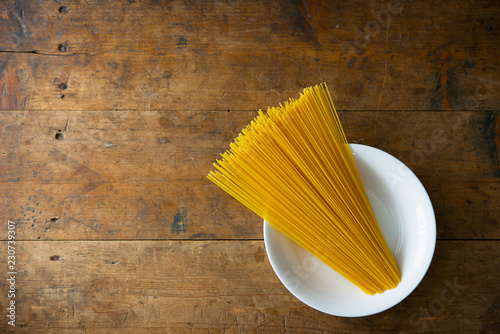 Bundle of long spaghetti on a white dish, placed on a old grungy wooden desk. photo