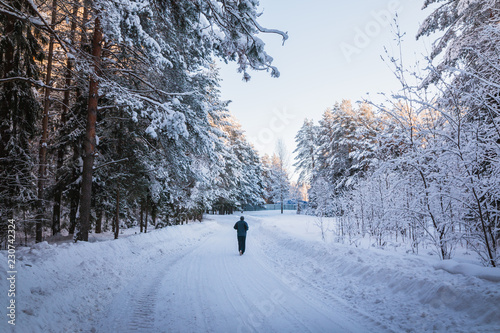 Runner on a snowy road surrounded by forest in a winter