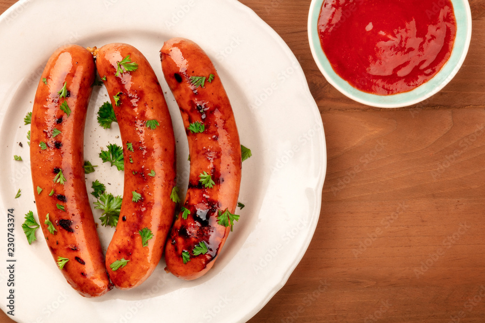 An overhead closeup photo of a plate of fried sausages, shot from above on a dark rustic wooden background with ketchup and copy space An overhead closeup photo of a plate of fried sausages, shot from above on a dark rustic wooden background with ketchup and copy space
